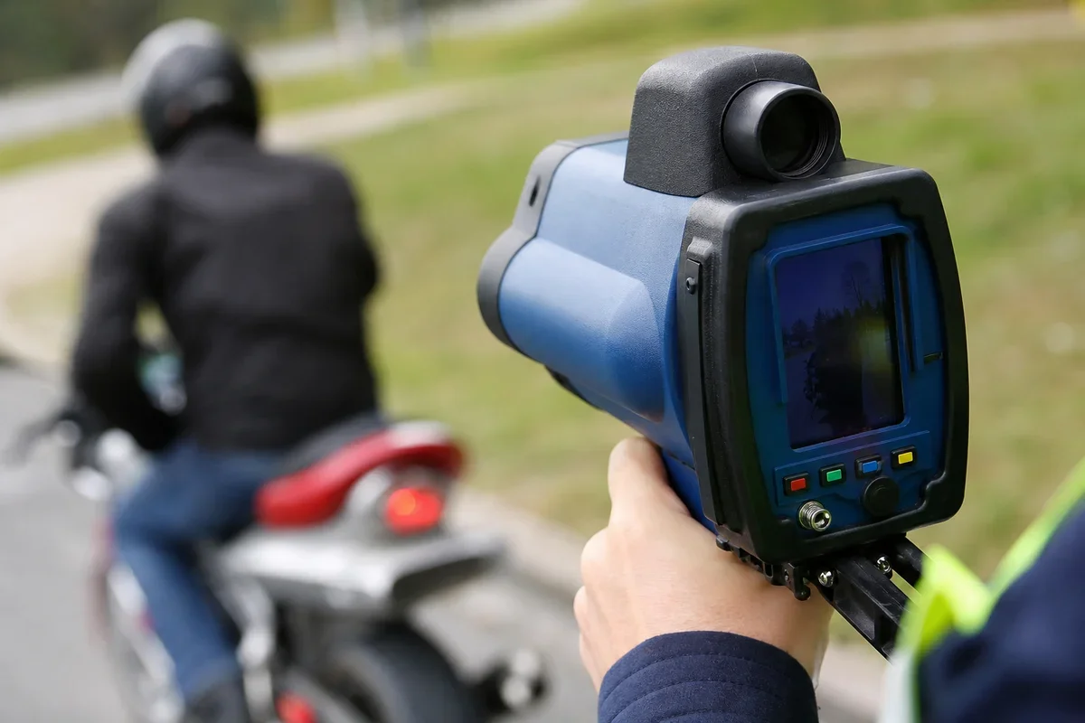 Funkcjonariusz mierzy prędkość jadącego motocyklisty za pomocą ręcznego radaru drogowego.